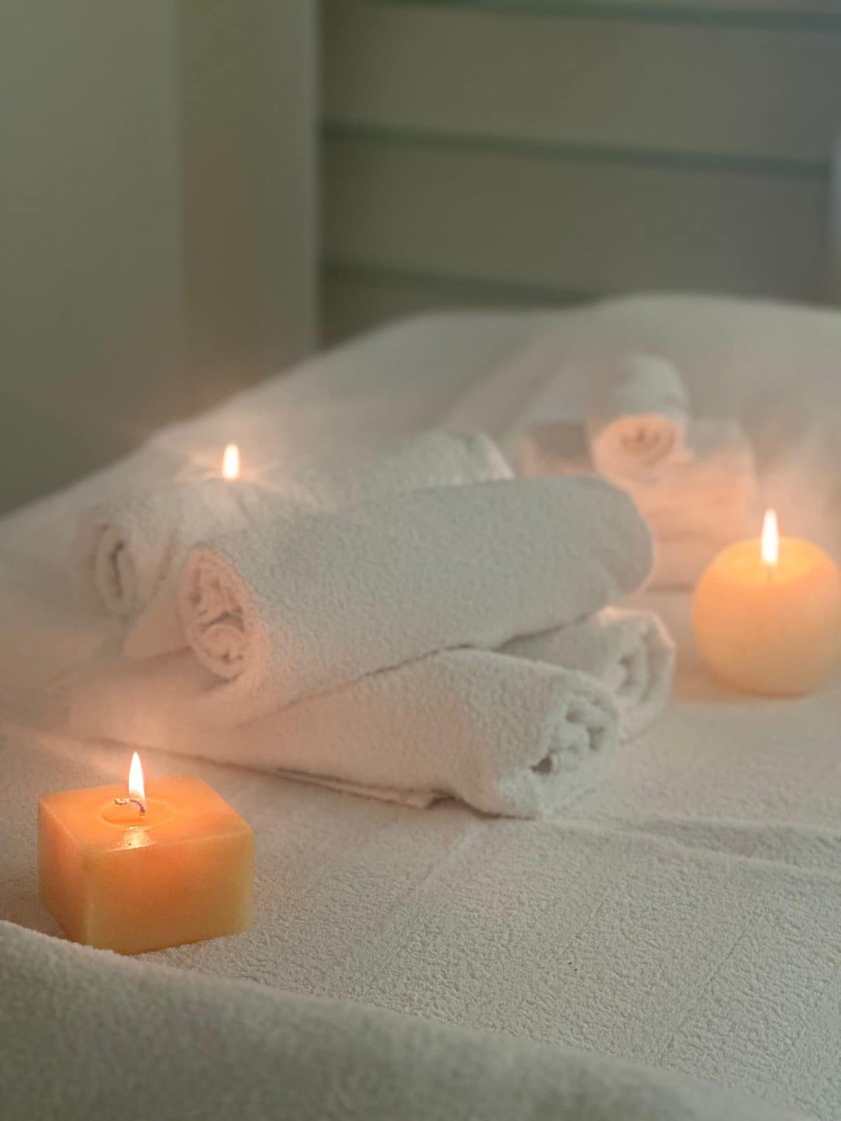 Lit candles beside rolled white towels in a treatment room at Oshun Beauty Spa