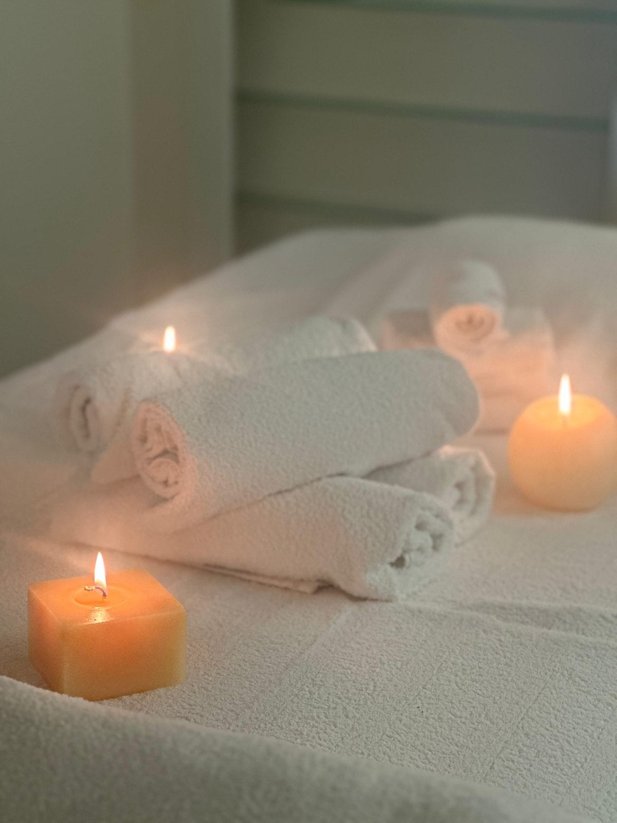 Lit candles beside rolled white towels in a treatment room at Oshun Beauty Spa